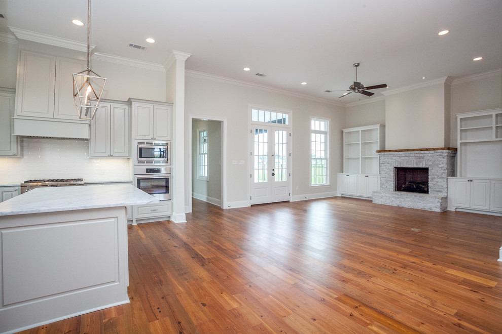 Mid-sized traditional open concept family room in New Orleans with beige walls, medium hardwood floors, a standard fireplace and a brick fireplace surround.
