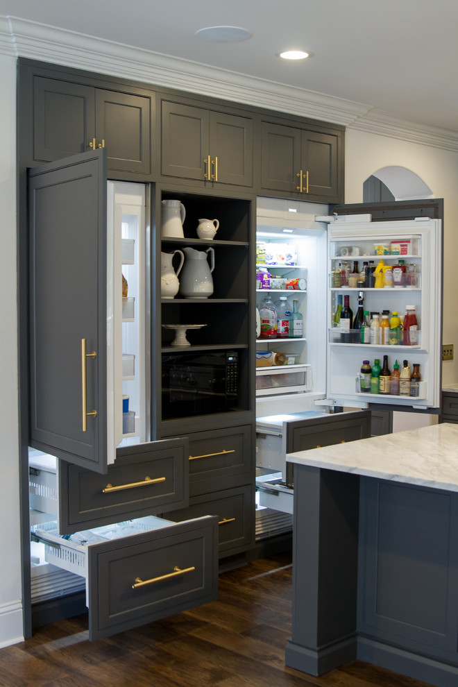 Example of a transitional medium tone wood floor and brown floor eat-in kitchen design with beaded inset cabinets, gray cabinets, white backsplash, paneled appliances, an island and white countertops