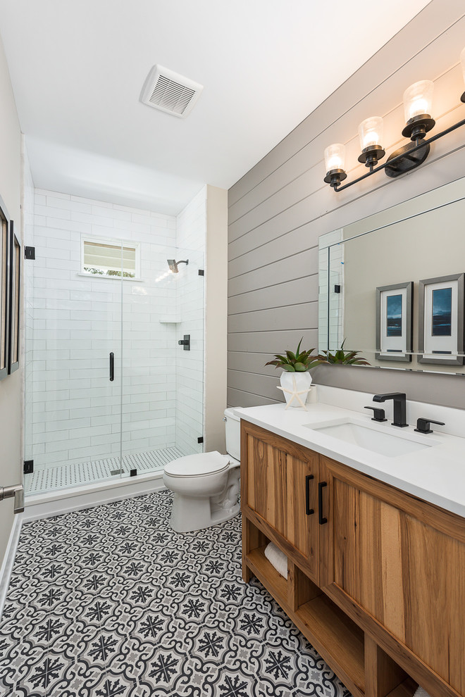Small country 3/4 bathroom in Chicago with shaker cabinets, medium wood cabinets, an alcove shower, a two-piece toilet, white tile, subway tile, beige walls, ceramic floors, an undermount sink, solid surface benchtops, multi-coloured floor, a hinged shower door and white benchtops.