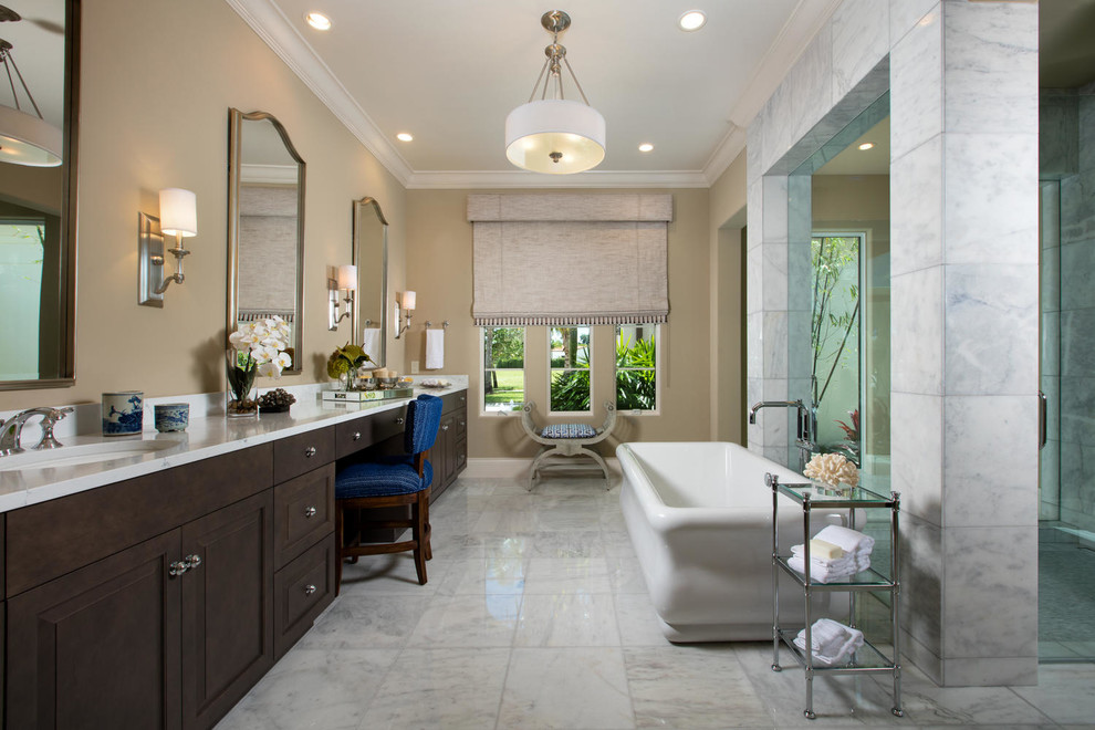 This is an example of a mediterranean master bathroom with raised-panel cabinets, brown cabinets, a freestanding tub, a curbless shower, gray tile, beige walls, an undermount sink and grey floor.