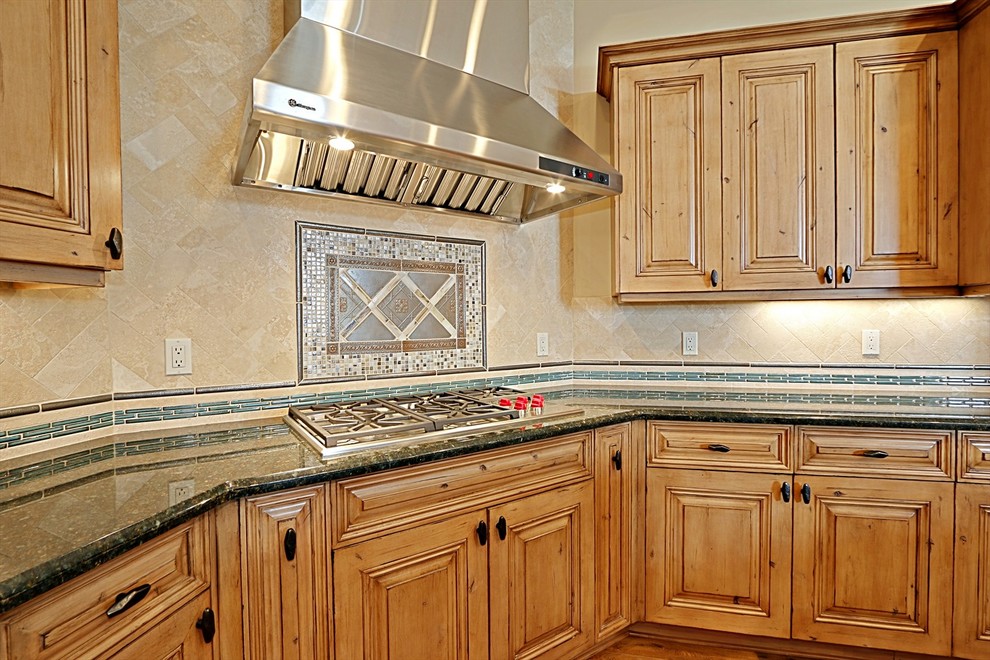 This is an example of a large kitchen in Phoenix with raised-panel cabinets, light wood cabinets, granite benchtops, beige splashback, panelled appliances, light hardwood floors and multiple islands.