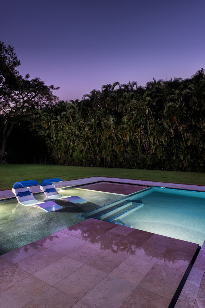 Large modern backyard l-shaped lap pool in Miami with a hot tub and natural stone pavers.