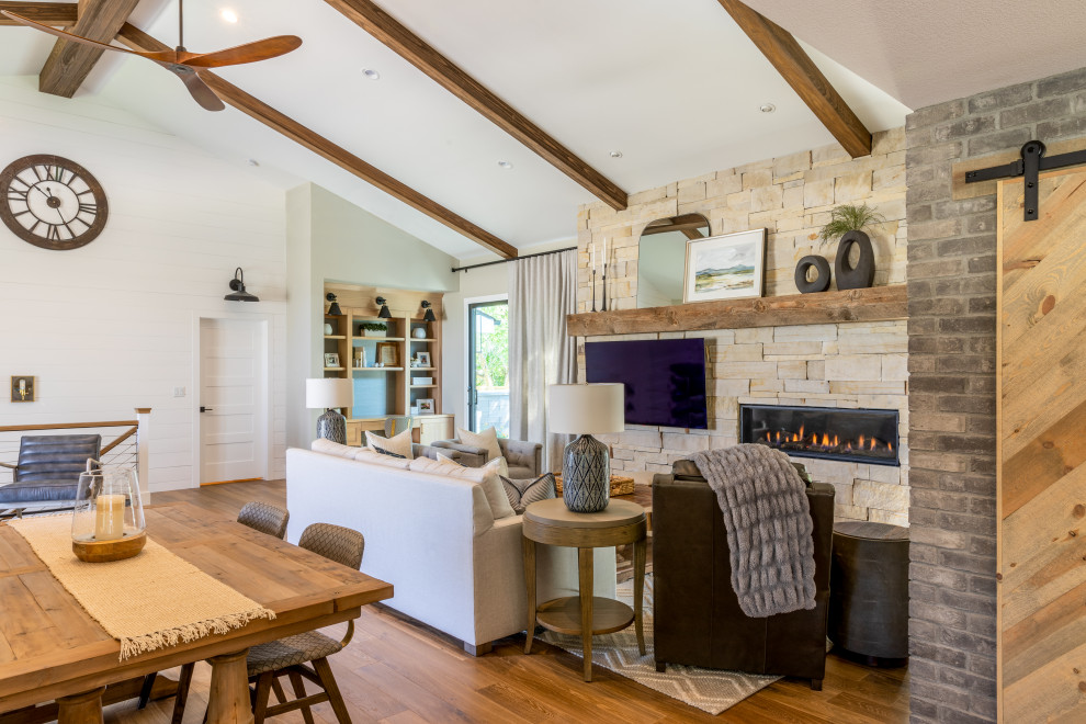Photo of a mid-sized country open concept living room in Denver with white walls, medium hardwood floors, a standard fireplace, a stone fireplace surround, a wall-mounted tv, brown floor, exposed beam and planked wall panelling.