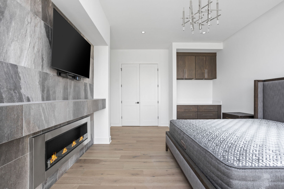 This is an example of a mid-sized contemporary master bedroom in Indianapolis with white walls, light hardwood floors, a hanging fireplace, a tile fireplace surround and multi-coloured floor.