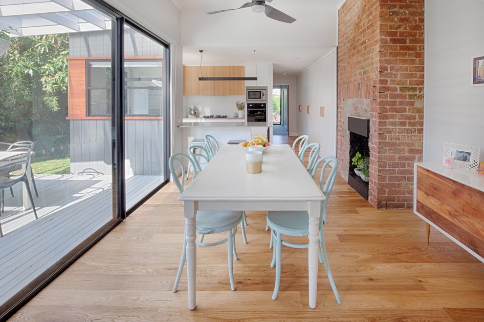Inspiration for a mid-sized contemporary kitchen/dining combo in Newcastle - Maitland with white walls, light hardwood floors, a brick fireplace surround, a standard fireplace and orange floor.