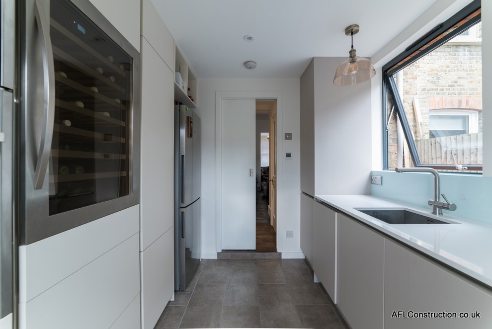 Inspiration for a mid-sized contemporary galley separate kitchen in London with a drop-in sink, flat-panel cabinets, white cabinets, solid surface benchtops, blue splashback, glass sheet splashback, stainless steel appliances, porcelain floors and no island.