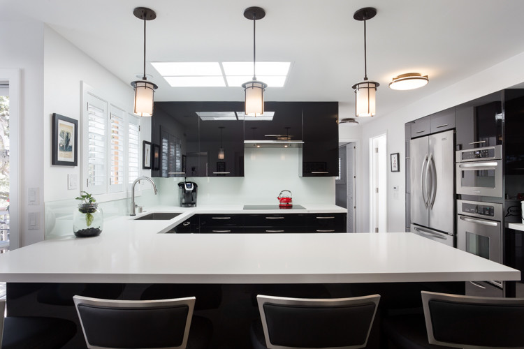 Inspiration for a contemporary u-shaped kitchen in San Francisco with flat-panel cabinets, black cabinets, white splashback, a peninsula, an undermount sink, glass sheet splashback and stainless steel appliances.
