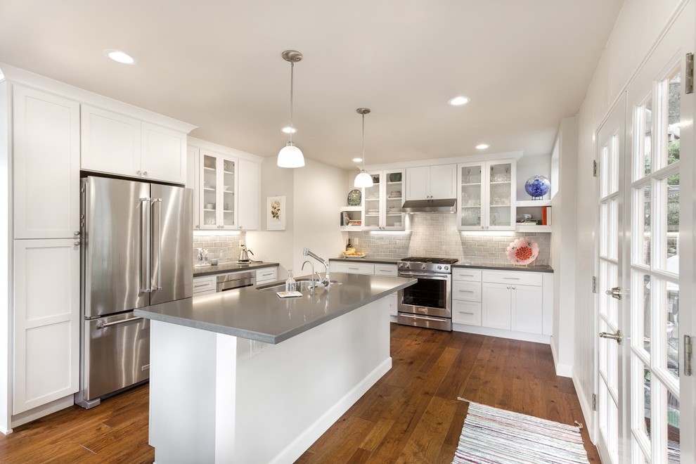Inspiration for a mid-sized transitional l-shaped medium tone wood floor eat-in kitchen remodel with an undermount sink, flat-panel cabinets, white cabinets, quartz countertops, gray backsplash, ceramic backsplash, stainless steel appliances and an island