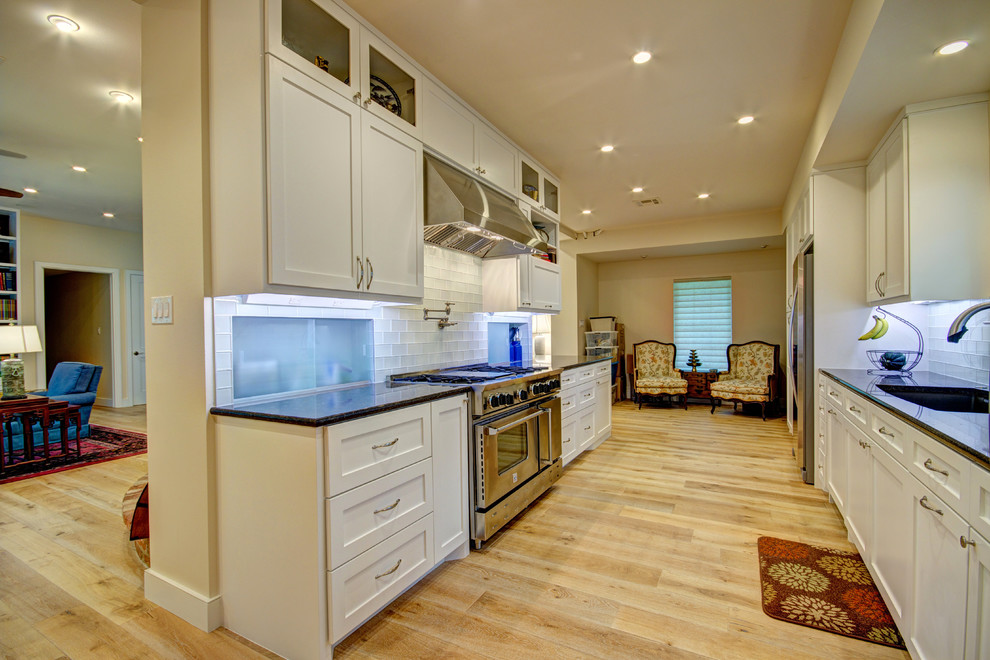 Eat-in kitchen - mid-sized transitional galley light wood floor eat-in kitchen idea in Austin with an undermount sink, shaker cabinets, white cabinets, granite countertops, white backsplash, glass tile backsplash, stainless steel appliances and no island