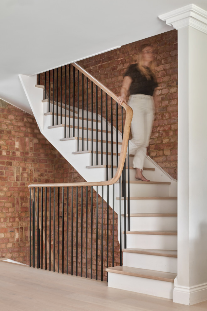 Mid-sized transitional wood curved staircase in London with metal railing and brick walls.