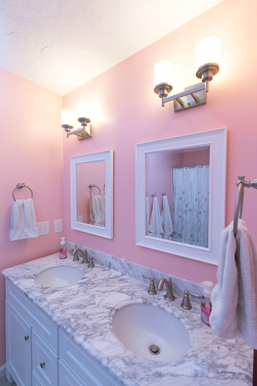 Photo of a small transitional kids bathroom in Cleveland with shaker cabinets, white cabinets, a shower/bathtub combo, a two-piece toilet, white tile, pink walls, porcelain floors, an undermount sink and engineered quartz benchtops.
