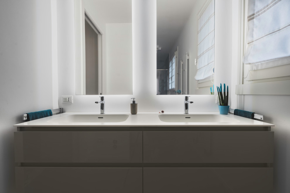 Пример оригинального дизайна: узкая и длинная ванная комната среднего размера в современном стиле с серыми фасадами, душем в нише, раздельным унитазом, синей плиткой, керамогранитной плиткой, белыми стенами, светлым паркетным полом, душевой кабиной, монолитной раковиной, столешницей из искусственного камня, бежевым полом, душем с раздвижными дверями, белой столешницей, тумбой под две раковины и подвесной тумбой