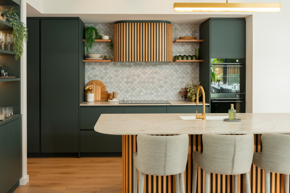 This is an example of a medium sized beach style galley kitchen pantry in Auckland with a submerged sink, flat-panel cabinets, green cabinets, quartz worktops, white splashback, marble splashback, black appliances, light hardwood flooring, an island, yellow floors and white worktops.