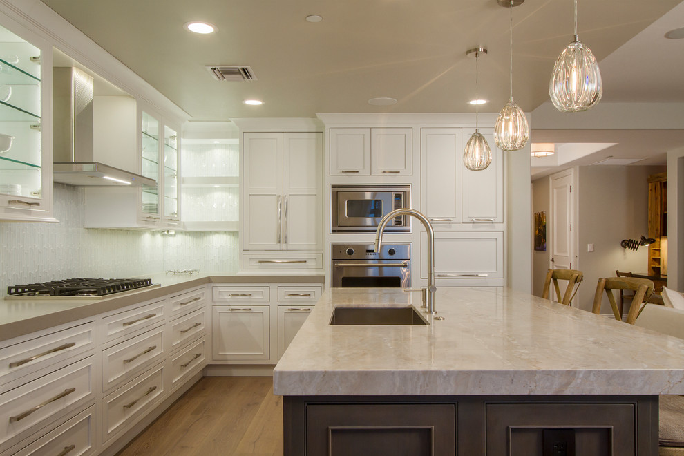 Inspiration for a small transitional l-shaped light wood floor and brown floor eat-in kitchen remodel in Phoenix with a single-bowl sink, shaker cabinets, white cabinets, quartz countertops, white backsplash, glass tile backsplash, stainless steel appliances, an island and white countertops