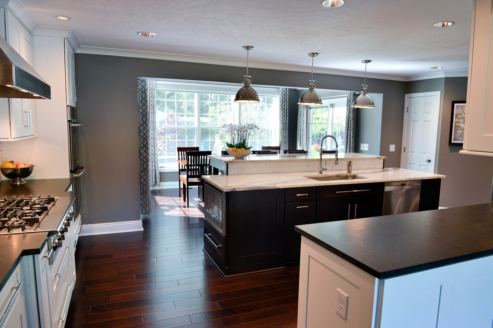 Inspiration for a transitional dark wood floor kitchen remodel in Cleveland with a drop-in sink, recessed-panel cabinets, white backsplash, ceramic backsplash, stainless steel appliances and an island