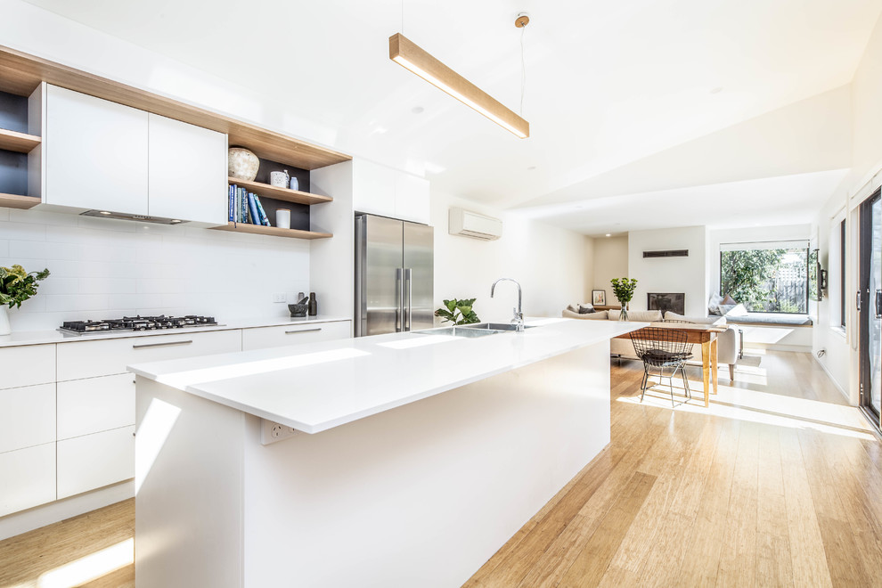 This is an example of a mid-sized contemporary galley open plan kitchen in Canberra - Queanbeyan with white cabinets, quartz benchtops, white splashback, subway tile splashback, stainless steel appliances, light hardwood floors, with island, beige floor, white benchtop and an undermount sink.