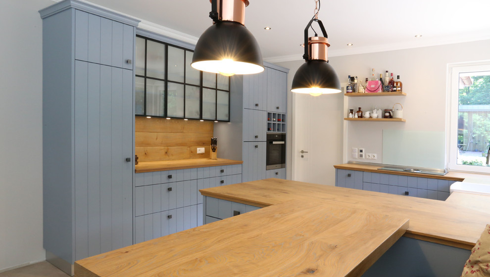 Inspiration for a large country u-shaped open plan kitchen in Bremen with raised-panel cabinets, blue cabinets, wood benchtops, glass sheet splashback, black appliances, a peninsula, brown benchtop, a farmhouse sink, beige splashback and porcelain floors.