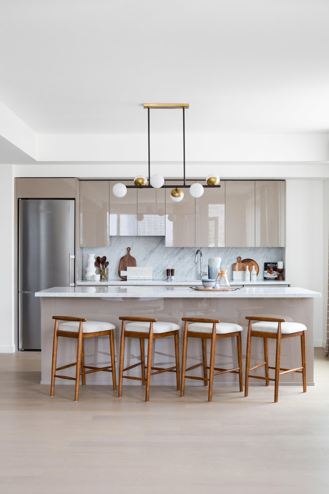 Design ideas for a large midcentury single-wall open plan kitchen in Los Angeles with flat-panel cabinets, beige cabinets, grey splashback, marble splashback, stainless steel appliances, light hardwood floors, with island, an undermount sink, marble benchtops and beige floor.