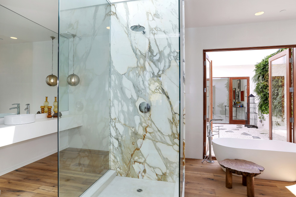 Inspiration for a large modern master bathroom in Los Angeles with white cabinets, a freestanding tub, a one-piece toilet, white tile, white walls, medium hardwood floors, a vessel sink, brown floor, a hinged shower door, an enclosed toilet, a double vanity and a floating vanity.