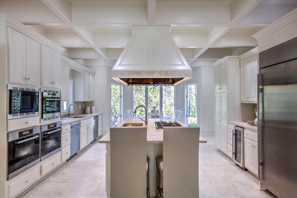 Inspiration for a large traditional galley open plan kitchen in Atlanta with a single-bowl sink, raised-panel cabinets, white cabinets, limestone benchtops, beige splashback, limestone splashback, stainless steel appliances, limestone floors, with island, beige floor and beige benchtop.