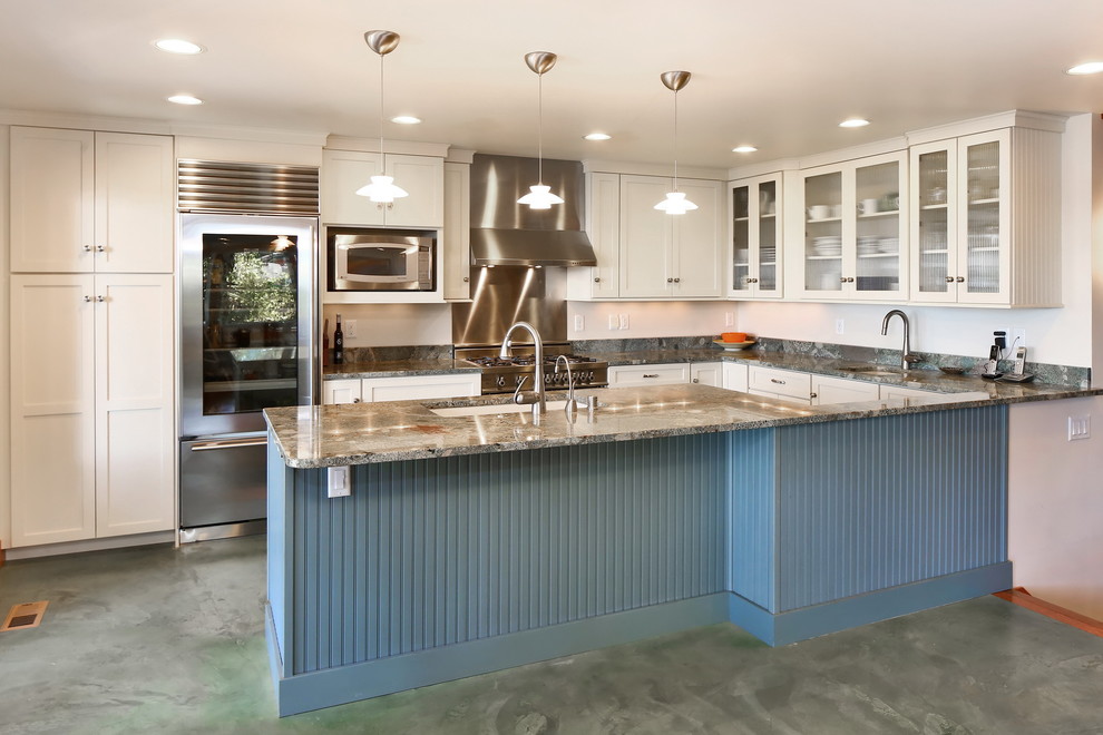 Inspiration for a beach style kitchen in Seattle with an undermount sink, glass-front cabinets, white cabinets, granite benchtops, grey splashback, stone slab splashback, stainless steel appliances, concrete floors, a peninsula, green floor and grey benchtop.