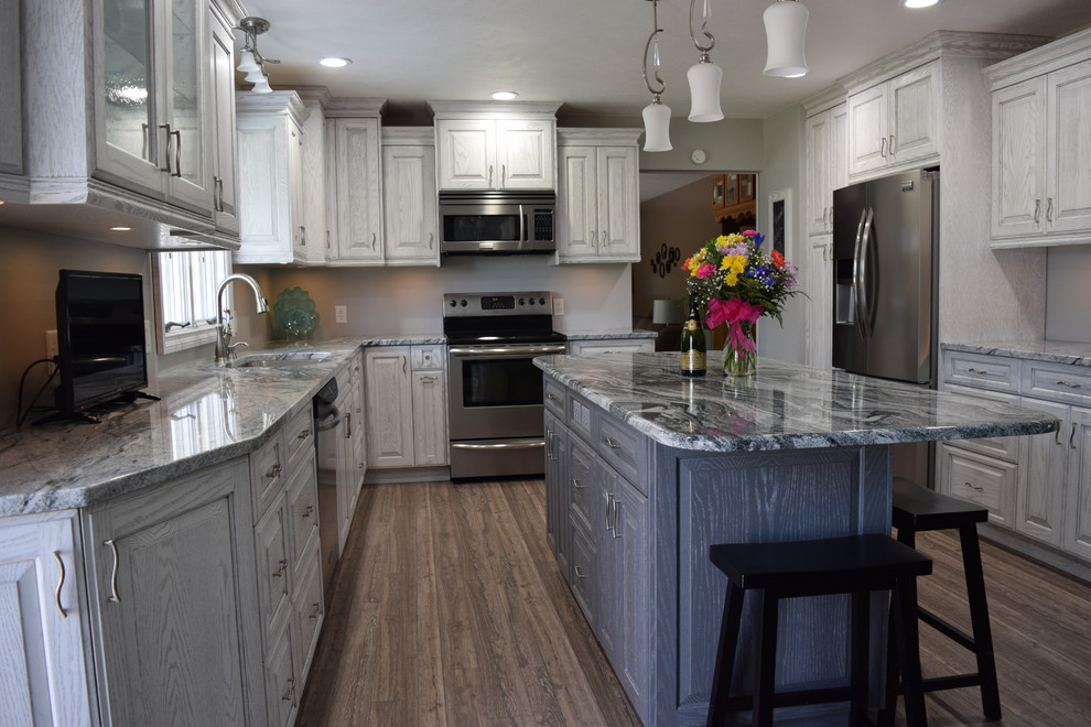This is an example of a mid-sized traditional l-shaped separate kitchen in Other with raised-panel cabinets, distressed cabinets, granite benchtops, stainless steel appliances, medium hardwood floors, with island and brown floor.