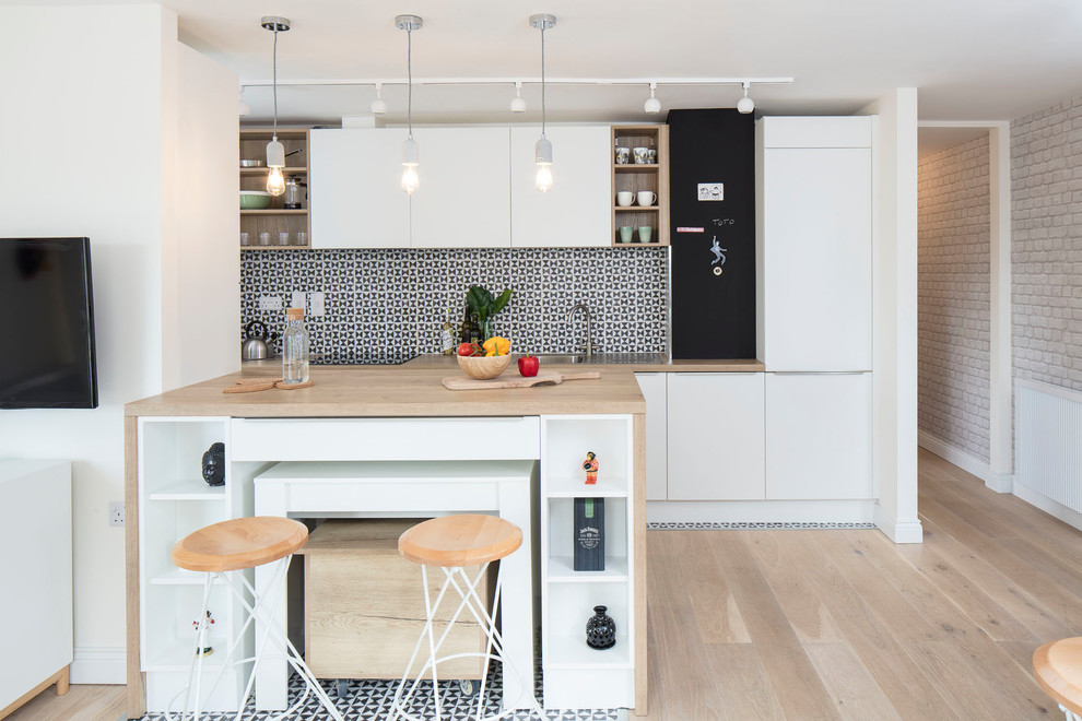 This is an example of a mid-sized scandinavian galley open plan kitchen in Dublin with flat-panel cabinets, white cabinets, laminate benchtops, multi-coloured splashback, porcelain splashback, panelled appliances, porcelain floors, a peninsula, beige floor and a drop-in sink.