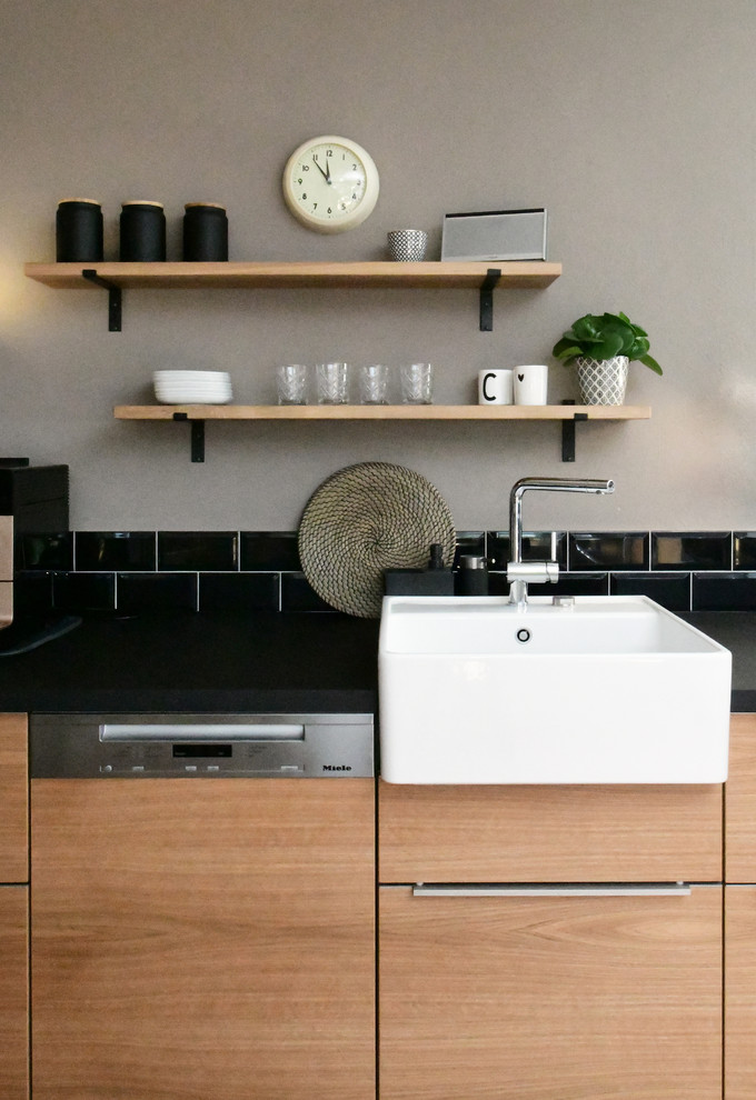 Inspiration for a mid-sized industrial l-shaped open plan kitchen in Frankfurt with a single-bowl sink, flat-panel cabinets, medium wood cabinets, wood benchtops, black splashback, subway tile splashback, stainless steel appliances, terra-cotta floors, a peninsula, red floor and black benchtop.