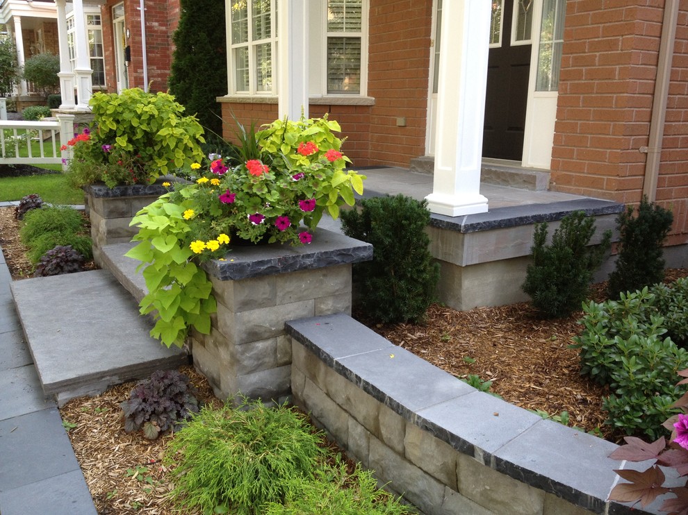 Photo of a small contemporary front yard shaded driveway for fall in Toronto with a retaining wall and natural stone pavers.
