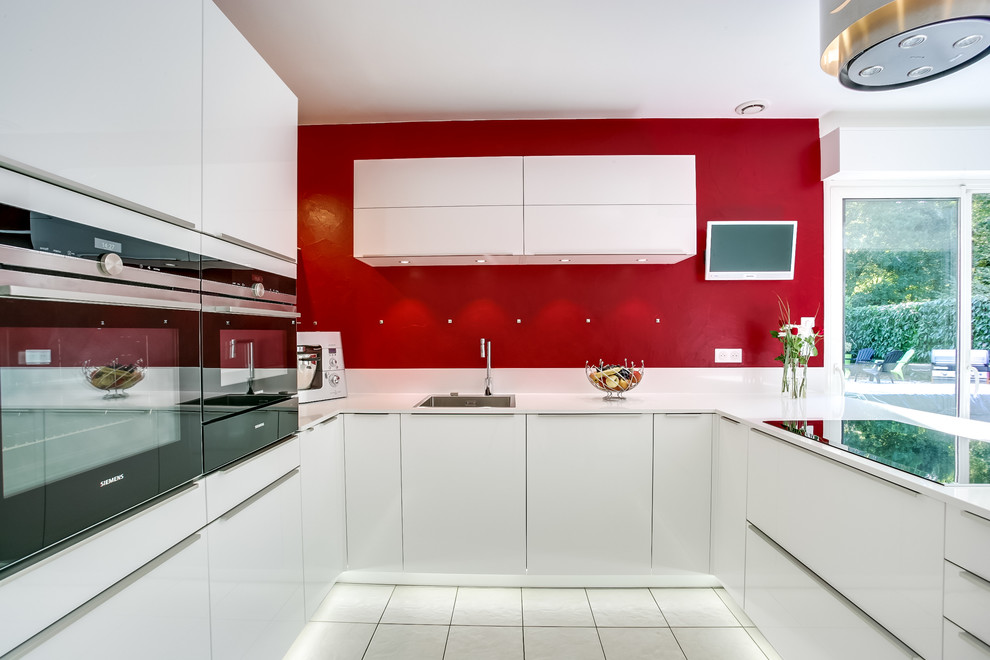 Mid-sized contemporary u-shaped eat-in kitchen in Paris with an undermount sink, flat-panel cabinets, white cabinets, red splashback and white appliances.