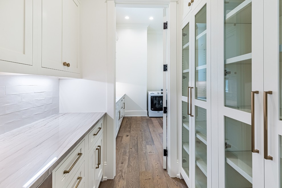 Inspiration for a mid-sized country laundry room with glass-front cabinets, white cabinets, white walls, medium hardwood floors and grey benchtop.