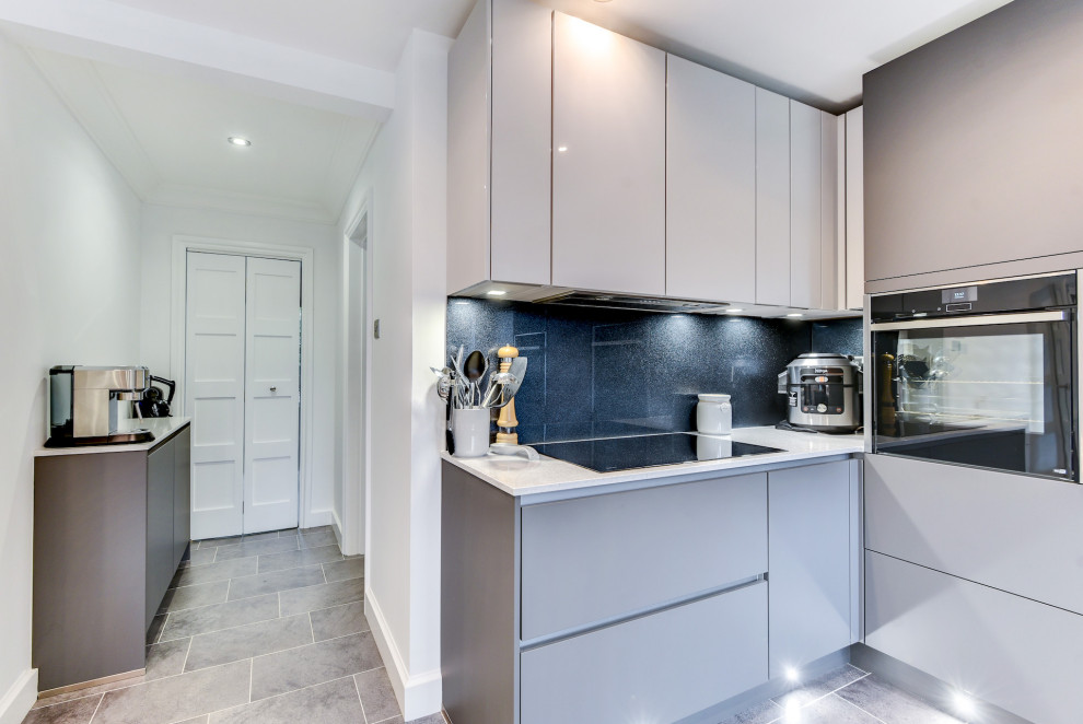 Large modern u-shaped open plan kitchen in Sussex with an undermount sink, flat-panel cabinets, grey cabinets, quartzite benchtops, grey splashback, glass sheet splashback, panelled appliances, vinyl floors, a peninsula, grey floor and white benchtop.