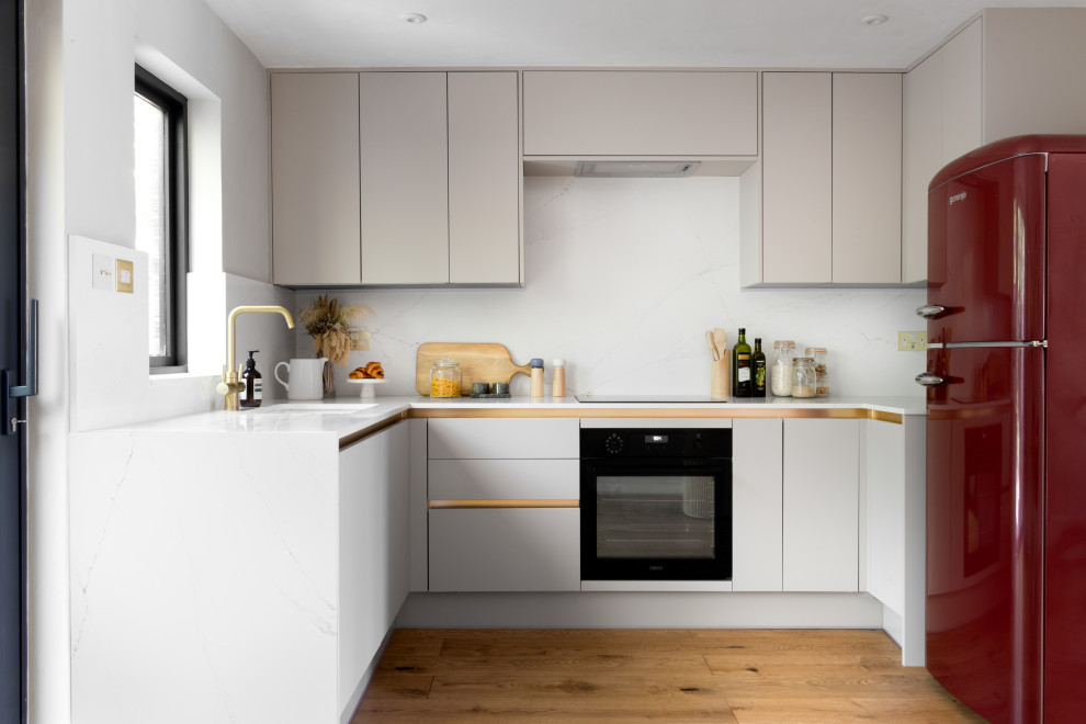 This is an example of a small contemporary u-shaped open plan kitchen in Manchester with an integrated sink, flat-panel cabinets, beige cabinets, solid surface benchtops, white splashback, black appliances, light hardwood floors, no island and yellow benchtop.