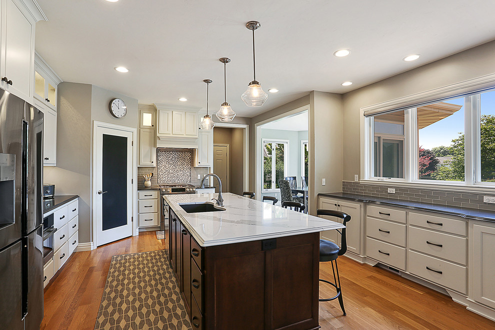 Kitchen - galley medium tone wood floor and brown floor kitchen idea with white cabinets, multicolored backsplash, stainless steel appliances, an island, an undermount sink and mosaic tile backsplash