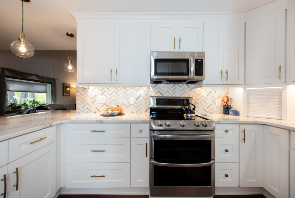 Inredning av ett klassiskt mellanstort vit vitt kök, med en undermonterad diskho, skåp i shakerstil, vita skåp, bänkskiva i kvarts, beige stänkskydd, stänkskydd i marmor, rostfria vitvaror, mörkt trägolv, en halv köksö och brunt golv