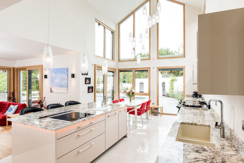 Photo of a large transitional open plan kitchen in Cambridgeshire with a double-bowl sink, flat-panel cabinets, beige cabinets, granite benchtops, with island, white floor and multi-coloured benchtop.