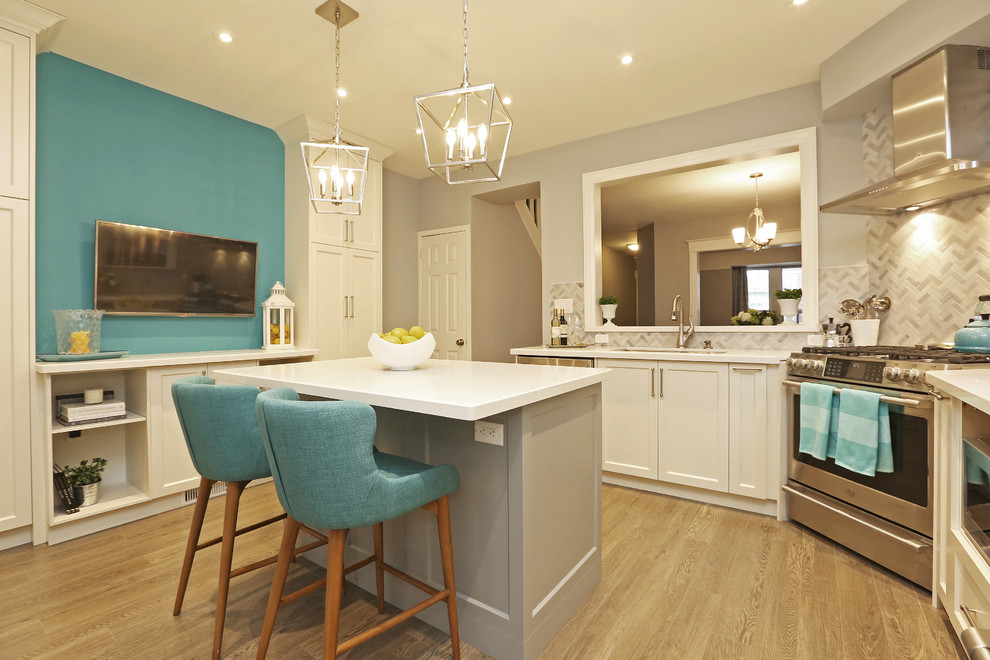 Example of a mid-sized transitional u-shaped light wood floor and brown floor enclosed kitchen design in Toronto with an undermount sink, shaker cabinets, white cabinets, solid surface countertops, gray backsplash, stainless steel appliances, an island and white countertops