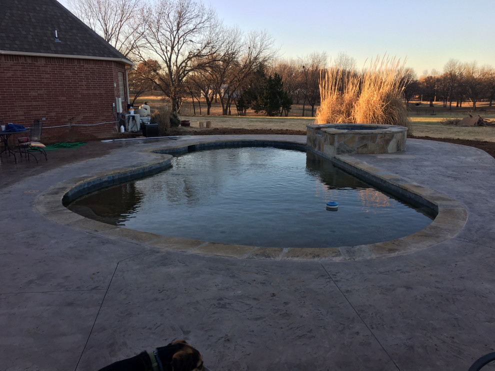 Design ideas for a mid-sized backyard custom-shaped natural pool in Oklahoma City with stamped concrete.