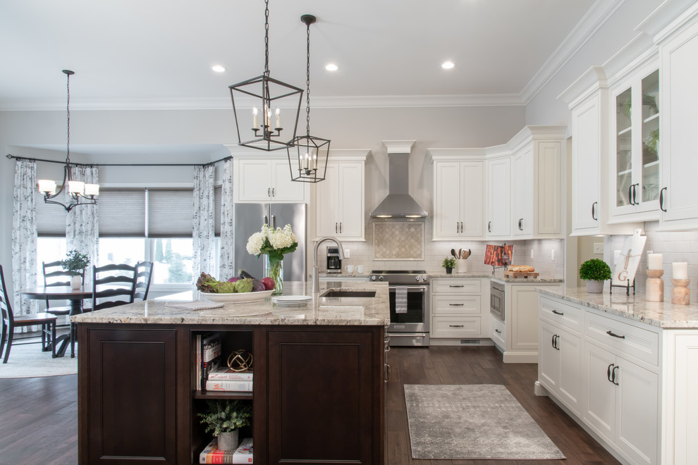 Transitional l-shaped kitchen in St Louis with an undermount sink, recessed-panel cabinets, white cabinets, white splashback, subway tile splashback, dark hardwood floors, with island, brown floor and grey benchtop.