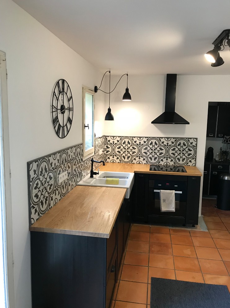 This is an example of a mid-sized midcentury l-shaped open plan kitchen in Marseille with an undermount sink, beaded inset cabinets, dark wood cabinets, wood benchtops, multi-coloured splashback, cement tile splashback, black appliances, terra-cotta floors, no island and orange floor.