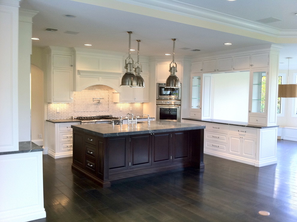 Large transitional u-shaped dark wood floor and brown floor open concept kitchen photo in Miami with a farmhouse sink, shaker cabinets, white cabinets, granite countertops, multicolored backsplash, stone tile backsplash, stainless steel appliances and an island