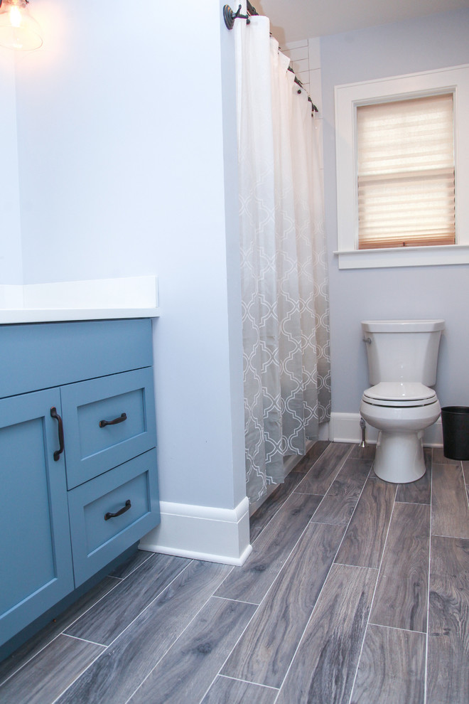 Photo of a mid-sized transitional kids bathroom in New York with furniture-like cabinets, blue cabinets, an alcove tub, a shower/bathtub combo, a two-piece toilet, grey walls, ceramic floors, an undermount sink, white tile and ceramic tile.