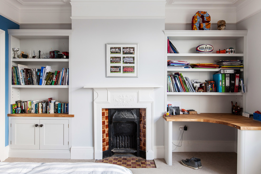 Mid-sized contemporary study room in Kent with white walls, carpet, a standard fireplace, a tile fireplace surround, a built-in desk and beige floor.