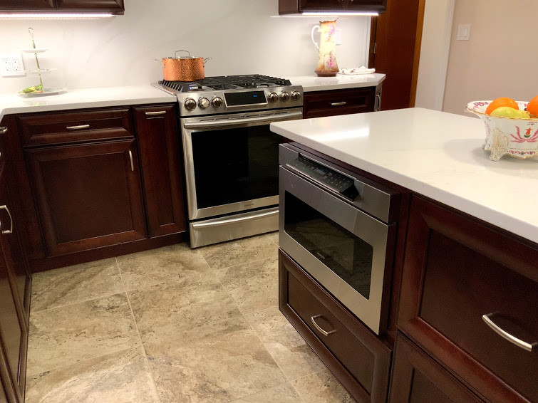 Photo of a large traditional l-shaped eat-in kitchen in New York with recessed-panel cabinets, dark wood cabinets, quartzite benchtops, white splashback, with island, grey floor and white benchtop.