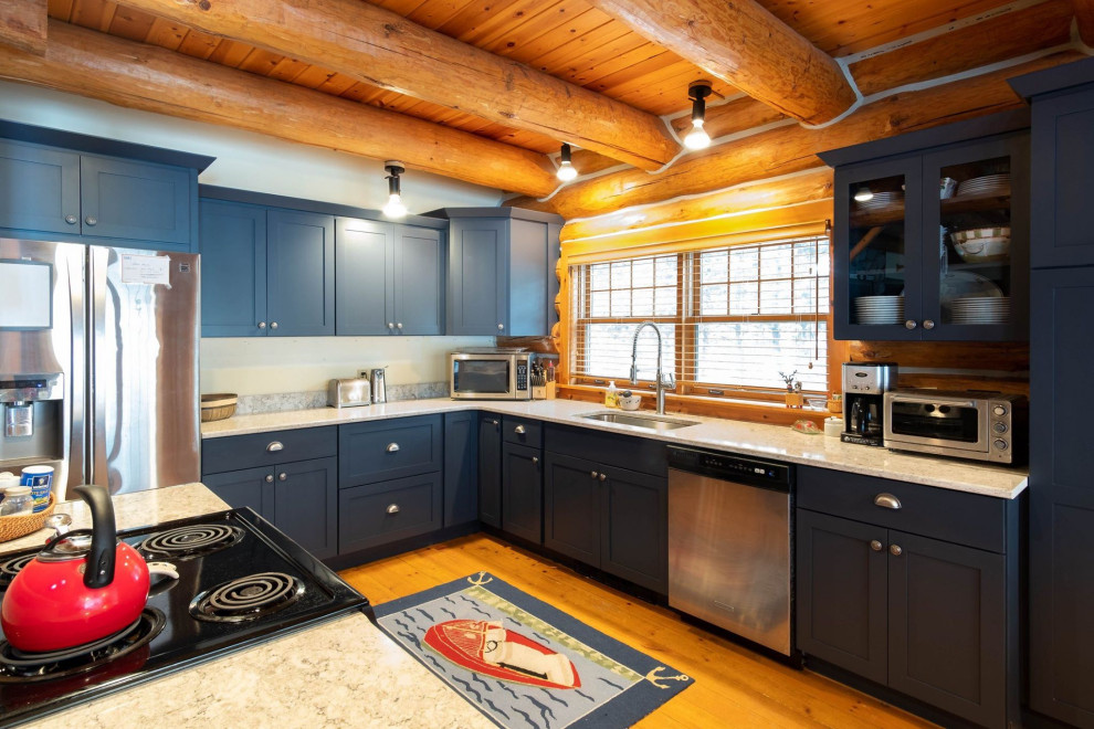 Photo of a beach style l-shaped eat-in kitchen in Other with an undermount sink, shaker cabinets, blue cabinets, quartz benchtops, beige splashback, stainless steel appliances, light hardwood floors, with island, brown floor and beige benchtop.