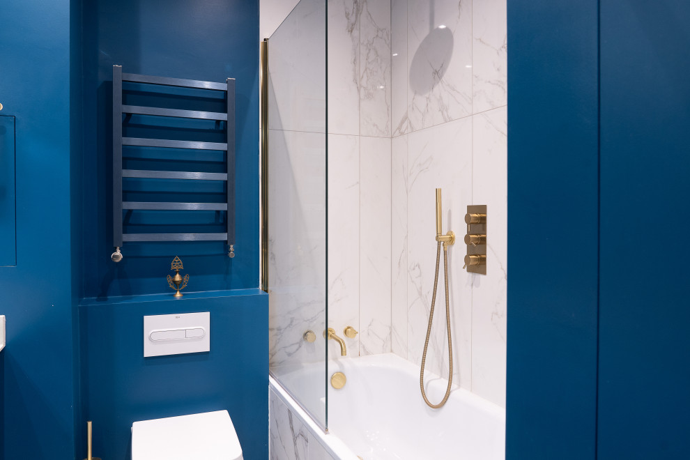 Photo of a mid-sized modern master bathroom in London with blue cabinets, an undermount tub, a wall-mount toilet, white tile, marble, blue walls, cement tiles, a trough sink, multi-coloured floor, a single vanity and a built-in vanity.