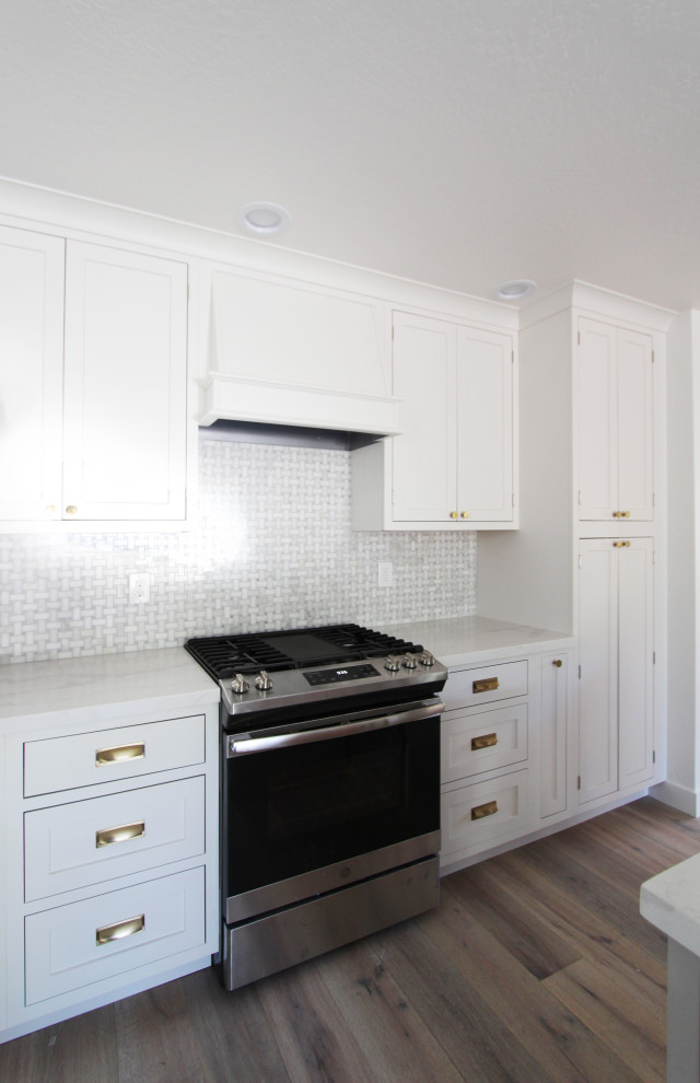 Inspiration for a mid-sized l-shaped light wood floor and brown floor open concept kitchen remodel with an undermount sink, shaker cabinets, white cabinets, quartz countertops, gray backsplash, mosaic tile backsplash, stainless steel appliances, an island and white countertops