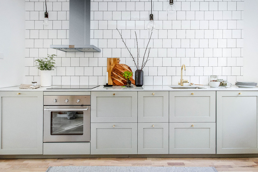 Inspiration for a large scandinavian single-wall kitchen in Stockholm with an undermount sink, shaker cabinets, grey cabinets, white splashback, subway tile splashback, stainless steel appliances, light hardwood floors and no island.