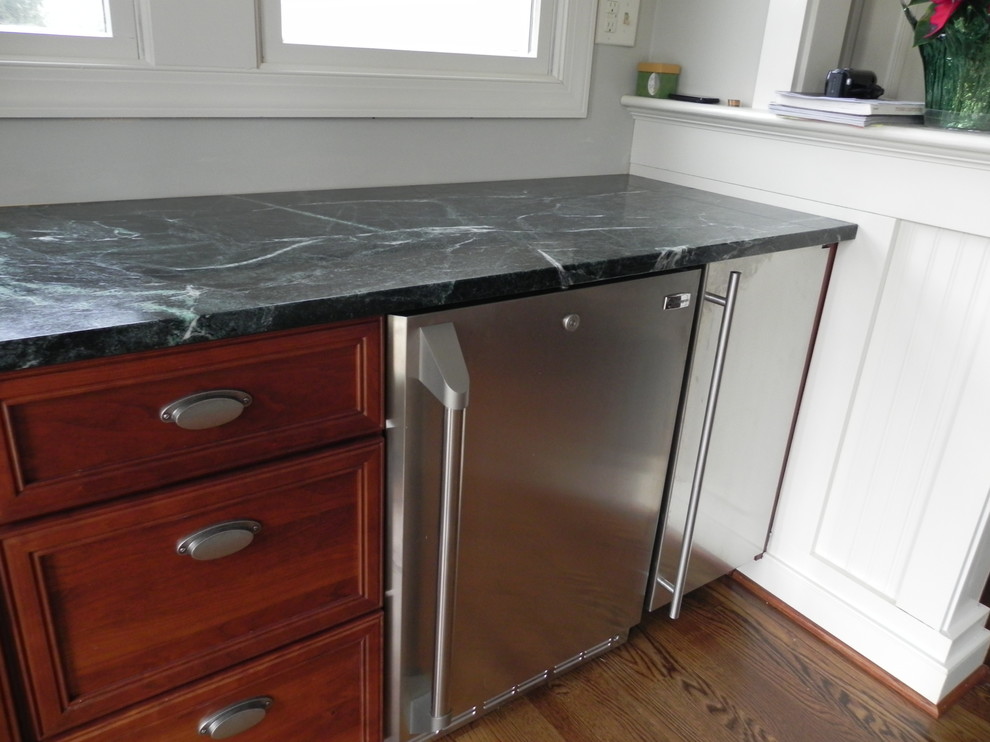 Photo of a mid-sized traditional single-wall open plan kitchen in Richmond with soapstone benchtops, recessed-panel cabinets, medium wood cabinets, stainless steel appliances and medium hardwood floors.