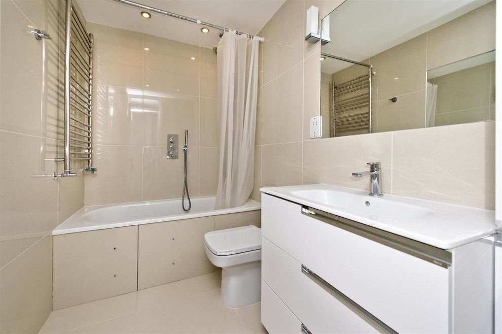 This is an example of a mid-sized contemporary master bathroom in London with an integrated sink, beaded inset cabinets, white cabinets, an alcove tub, a two-piece toilet, beige tile, porcelain tile, white walls and porcelain floors.